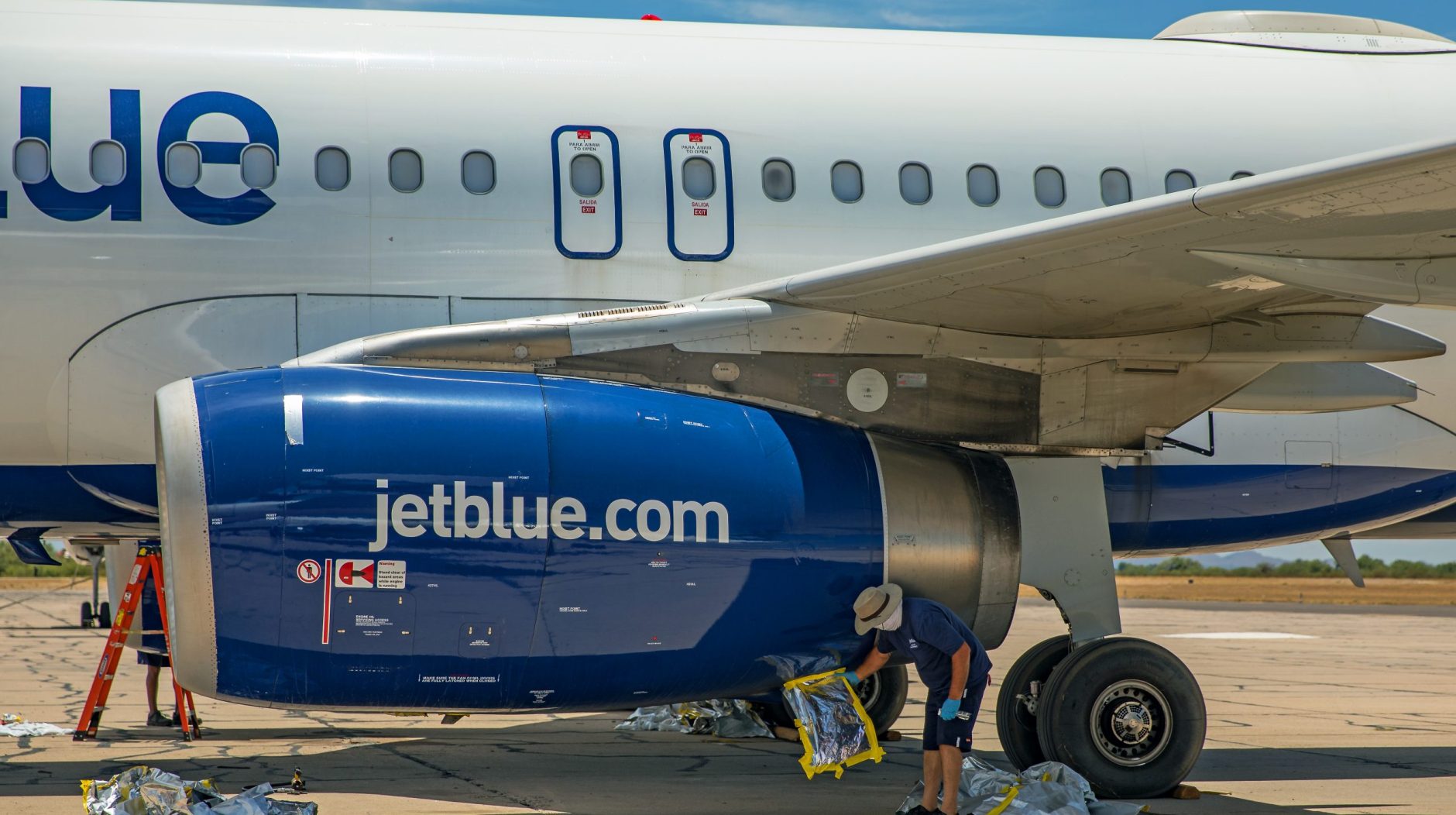 Maintenance crews remove engine covers from a JetBlue aircraft.